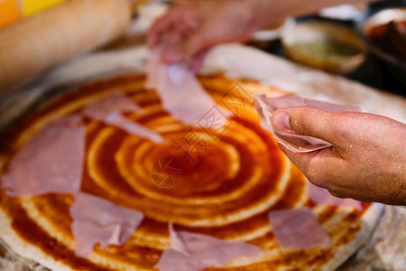 厨师把火腿放在比萨饼餐厅的面团上做饼的过程图片