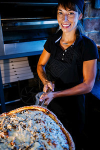 身着黑色制服的笑脸女厨师在披萨餐厅用木盘上拿着比萨饼图片