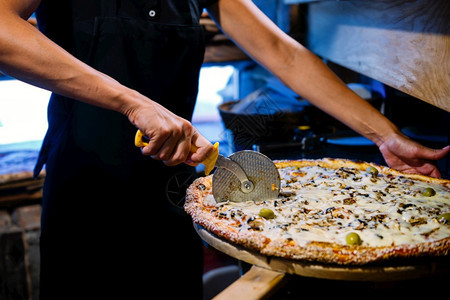 身穿黑色制服的女厨师穿着披萨和木皮上的披萨卷切刀图片