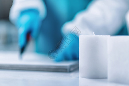 蜡烛制作者用手术刀切割白蜡穿着蓝色保护工作服图片