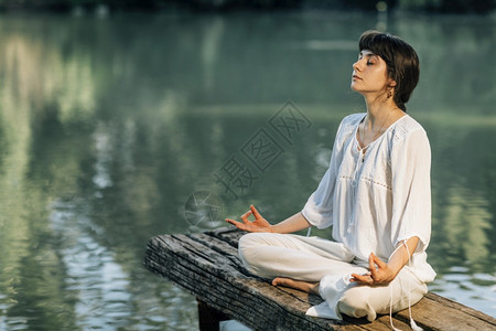 瑜伽后退宁静的年轻女子坐在莲花的位置上静地坐在湖边冥想图片