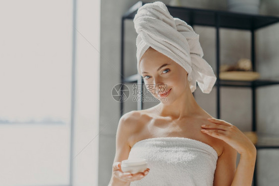 满意的年轻女照片有健康的纯皮肤施用体奶油利皮肤治疗来润湿用毛巾包着微笑轻地图片