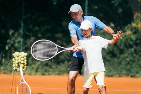 在粘土场上与网球教官一起训练男孩在网球场上训练男孩图片