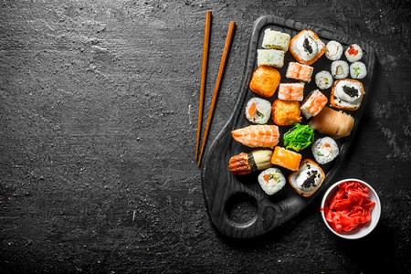 不同的寿司卷在切割板上黑色生锈背景图片