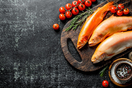含迷迭香料和西红柿的切菜板上生鱼鳟在含迷迭香料和西红柿的切菜板上生鱼鳟图片