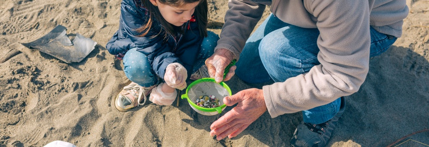 爷和孙女志愿者在海滩上拾取微塑料背景图片