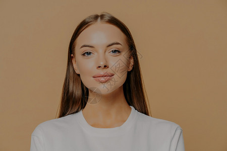 长头发的欧洲美女肖像自信摄影机健康光彩化妆穿着棕色工作室墙边的随意跳跃器美丽和健康的概念背景图片