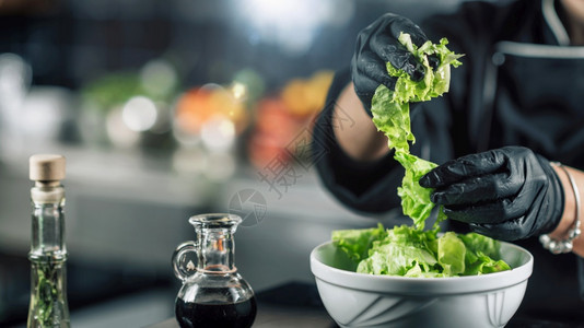 制作健康素食沙拉的女厨师和准备绿色沙拉的手背景图片