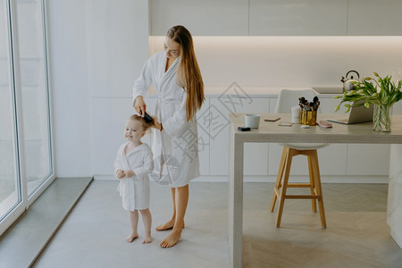 陪伴母亲身穿白色浴袍站在厨房给小孩梳头背景
