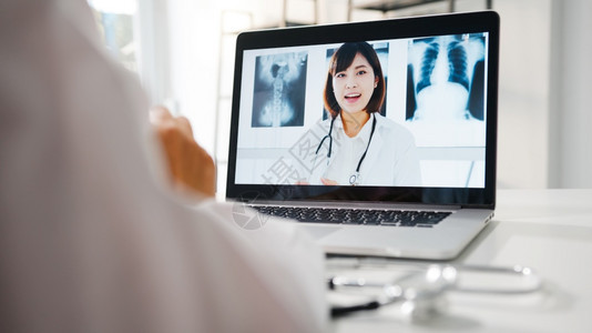 白制服的年轻女医生使用笔记本电脑交谈视频话在诊所或医院的书桌与高级医生交谈社会偏移冠状隔离图片