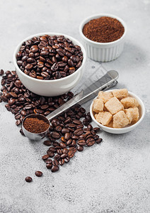 新鲜生有机咖啡豆以白碗和粉末制成以甘蔗和圆钢勺在桌边背景上图片