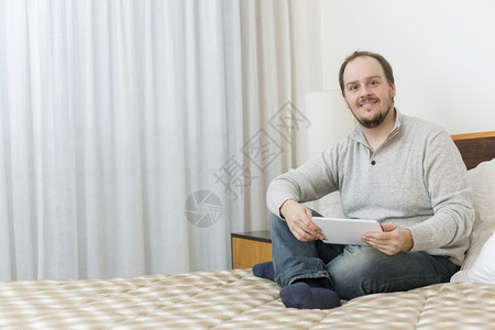 在床上用平板纸在床上工作的临时男子图片