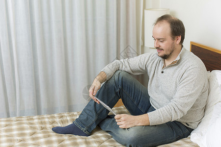 在床上用平板纸在床上工作的临时男子图片