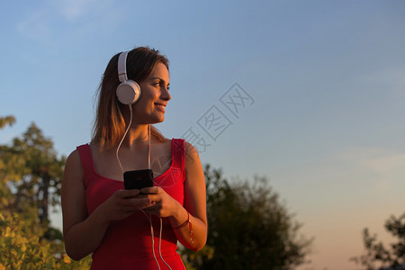 放音乐的女孩美丽的临时女在日落享受音乐用耳机在户外放背景