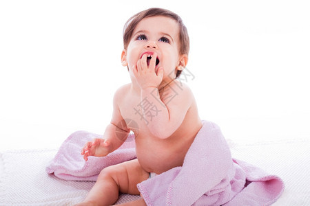 婴儿用张嘴笑坐在白色孤立背景的紫毛巾上图片