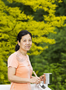 一位成年妇女在准备绿色自然背景的白木甲板上打栏时持有油漆罐和刷的垂直照片背景图片