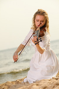 海滩上玩小提琴的金发女孩音乐爱好者的概念图片