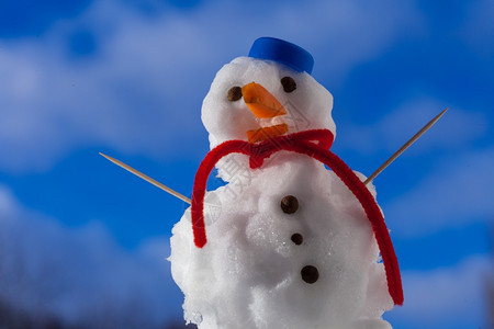 圣诞小雪人穿着蓝螺丝顶的戴红色帽子围巾露天有牙签冬季节蓝天空背景图片