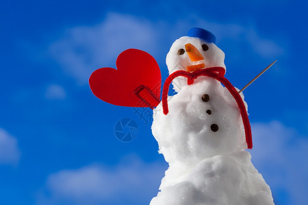 圣诞小雪人穿着蓝螺丝顶的色雪人帽子红围巾和心爱的短片符号牙签在户外冬季节特定情人39日蓝天空背景图片