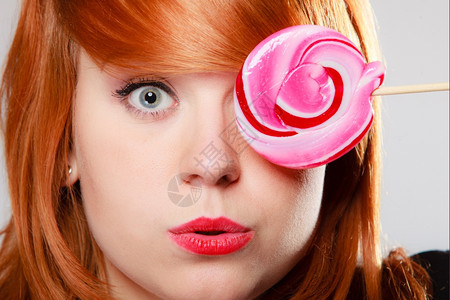 拿着糖果的有趣年轻女人红发孩粉色棒糖在取笑工作室拍甜图片