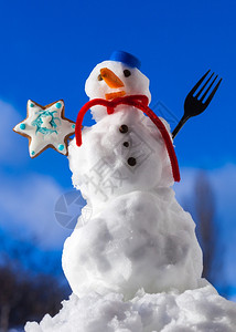 雪人穿着蓝螺丝顶作为帽子红围巾和有叉姜饼蛋糕干明星在户外冬季节特别蓝天空背景图片