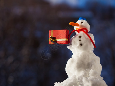 穿着蓝色螺丝顶上的小快乐雪人戴着帽子红围巾还有露天的叉子圣诞礼物盒冬季节特制模糊的背景图片