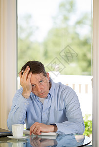 成年男子的垂直形象显示抑郁症一方面用只手握住头部另一方面在家工作光照日背景从窗户进来图片