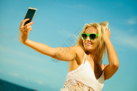 科技互联网旅游度假概念快乐的少女孩在海滩上用智能手机相自拍照背景图片