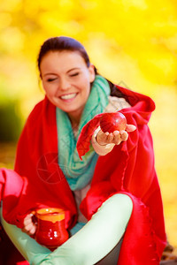 穿着红色毯子的女在秋天公园休息享受热饮提供苹果黄叶背景图片