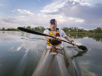 高级男正在一个平静的湖上划赛艇背景有暴云科罗拉多州柯林斯堡图片