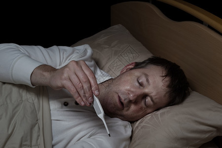 成年男子的水平图像读取温度计同时躺在床上图片