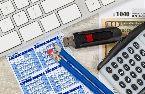 美国税表104计算器日历货币计算机拇指驱动器和木制桌面上的铅笔背景图片