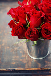 在木背景的花瓶里美丽红玫瑰图片