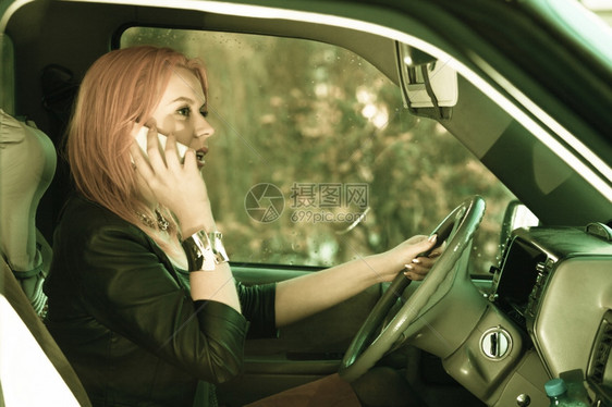 年轻女司机红发孩在开车时用手机智能电话说图片