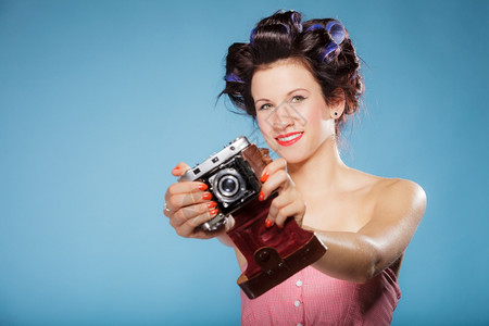 穿着头发卷的漂亮女孩用古老相机拍照片蓝色背景图片