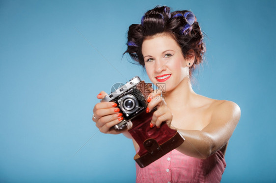穿着头发卷的漂亮女孩用古老相机拍照片蓝色背景图片