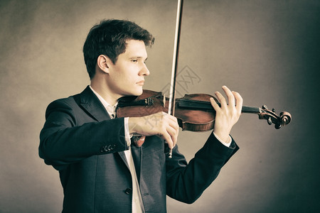 年轻优雅的小提琴家手在棕色和古典音乐上拉小提琴背景图片
