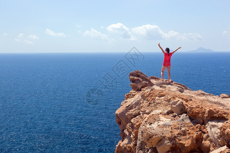 快乐的女士在摇滚上举起手来胜利成功积极旅行概念圣托里尼岛希腊胜利旅行概念图片