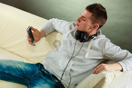 年轻英俊男子在家用耳机智能手在沙发上放松图片