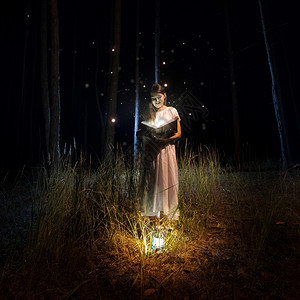 穿长裙的美女在神秘森林里读着大老书带萤火虫图片