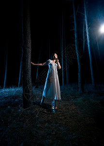 穿着白睡衣的单身女人看着夜林的光束图片
