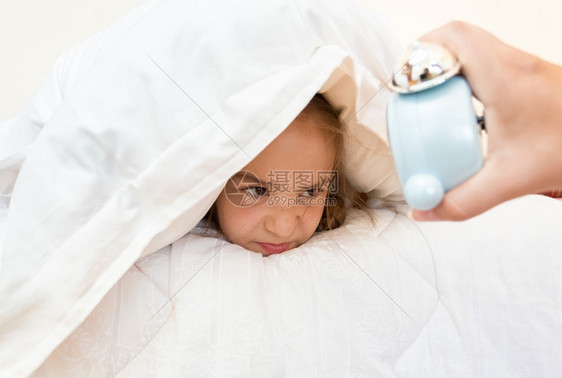 小女孩用枕头盖看着闹钟的肖像图片