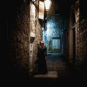穿着长黑色裙的感年轻女站在旧窄街灯笼下图片