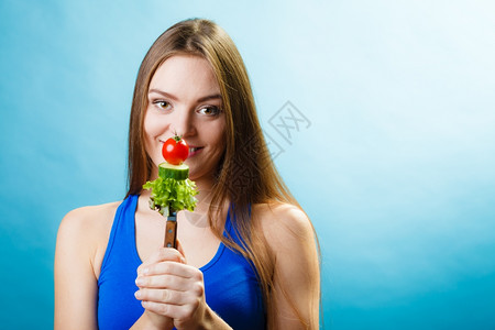 美食和减肥概念有趣的女孩健身人拿着叉子和新鲜混合蔬菜蓝色背景图片