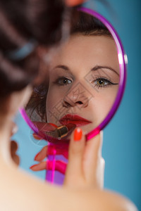 年轻女子准备参加聚会出去玩女孩用卷头发用红口涂看着镜子反光风格的蓝色背景图片