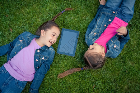 两个小女孩面对地躺在草上看着石板图片