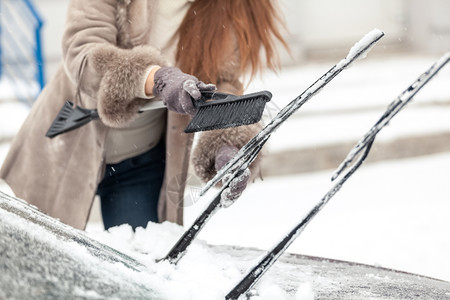 妇女从雪中用刷洗车擦器的近镜头图片