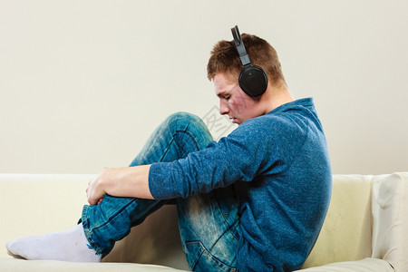 年轻的英俊男子带着耳机坐在沙发上集中地听音乐图片