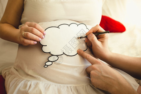 在Wife怀孕腹部的纸牌上写字男子照片剪贴图片
