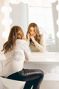 年轻时尚的女人看着她反光照有灯泡的镜子背景图片